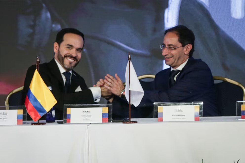 Abelardo de la Espriella y José Manuel Restrepo se estrechan las manos, sentados ante una mesa con banderas. José Manuel Restrepo en la ONU referencia.