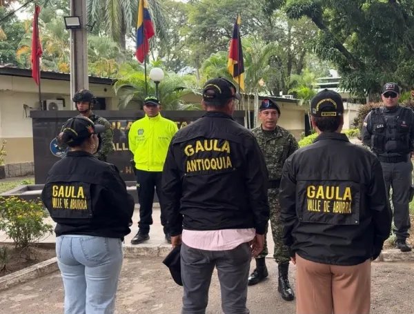 Tres personas de espaldas con chaquetas del Gaula frente a integrantes de las autoridades. Rescate en Gómez Plata.